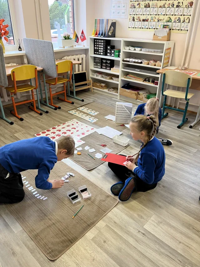 Vaikai kartu dirba su Montessori priemonėmis ant kilimėlių