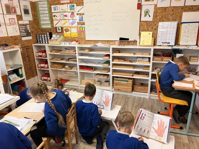 Mokiniai dirba Montessori klasėje, apsupti mokymosi priemonių